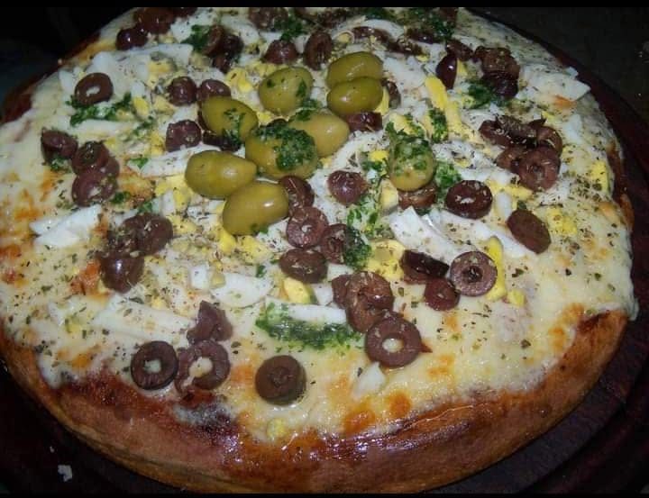 Pizza con huevo y aceitunas sobre tabla de madera